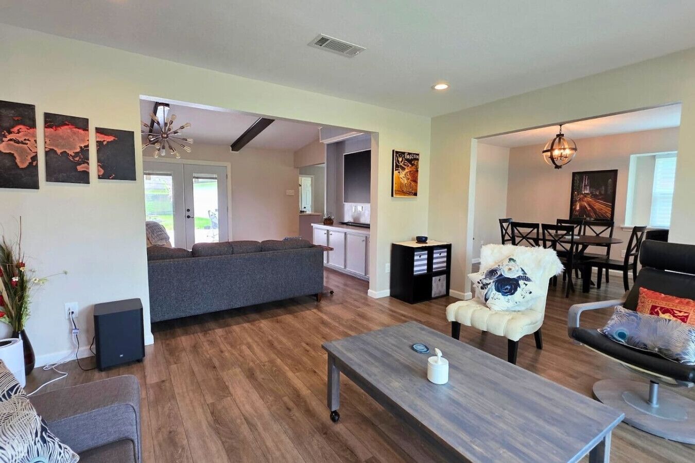 A spacious living room with a grey sofa, a coffee table, and a dining area with a chandelier.