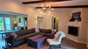 Uma sala de estar com sofá seccional, banquinho, poltrona, lareira e um lustre moderno.