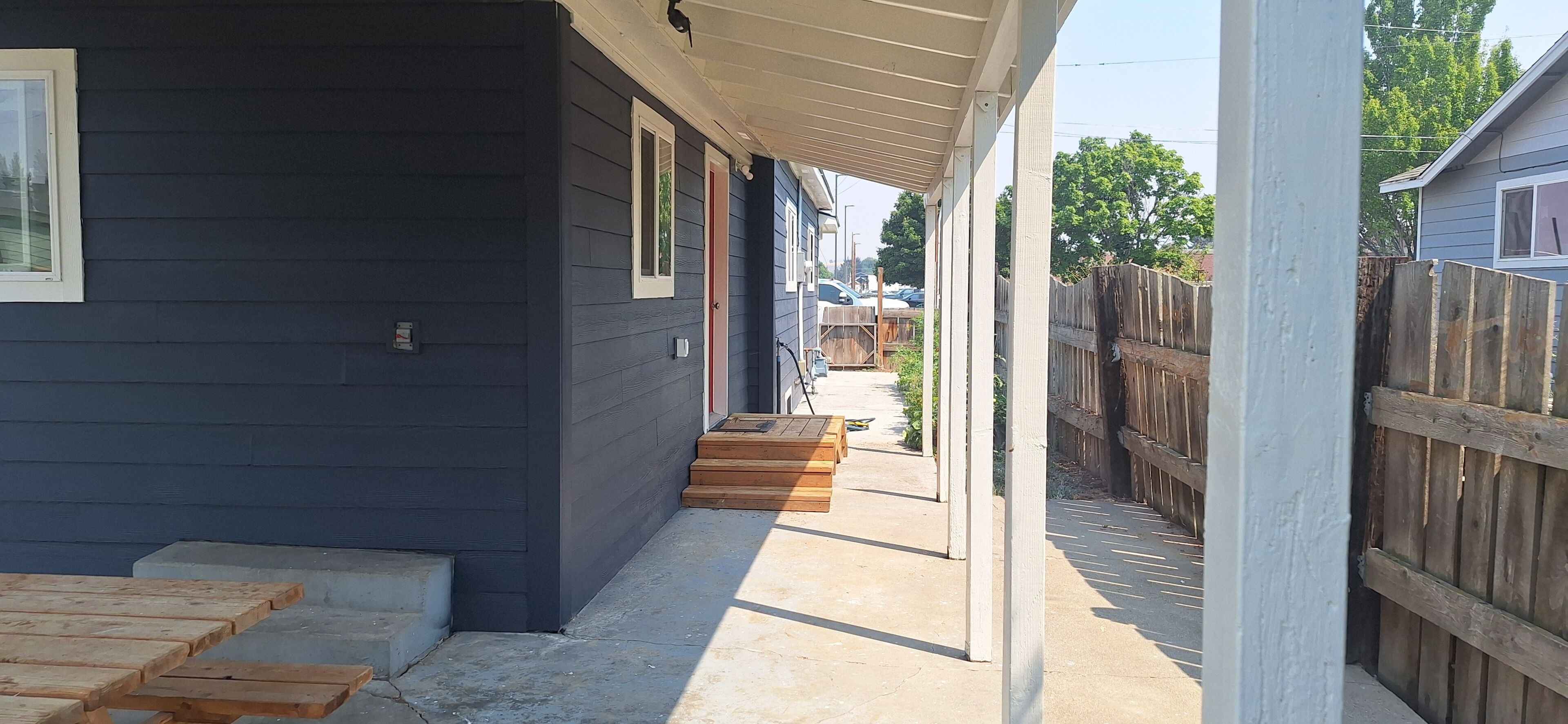 A covered porch with steps leading to a door, a wooden fence, and a clear sky.
