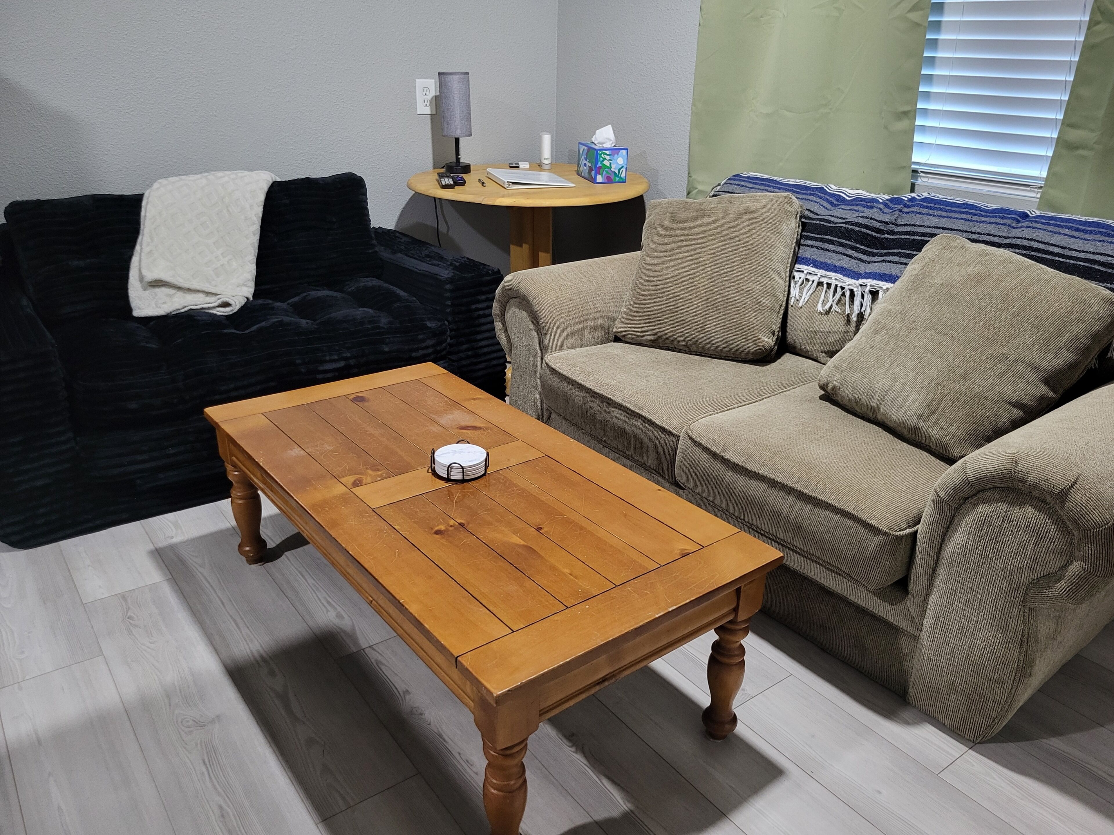 Ein Wohnzimmer mit einem Holztisch, einem schwarzen Sofa und einem beigen Sofa mit gestreiften Kissen.
