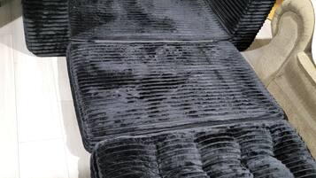 A black sofa with a textured surface, a wooden side table with a lamp, and a beige chair.