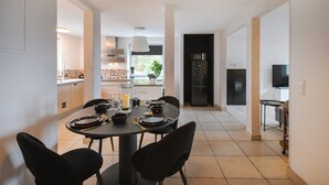 A modern dining area with a round table set for four, a kitchen in the background, and a TV in a corner.