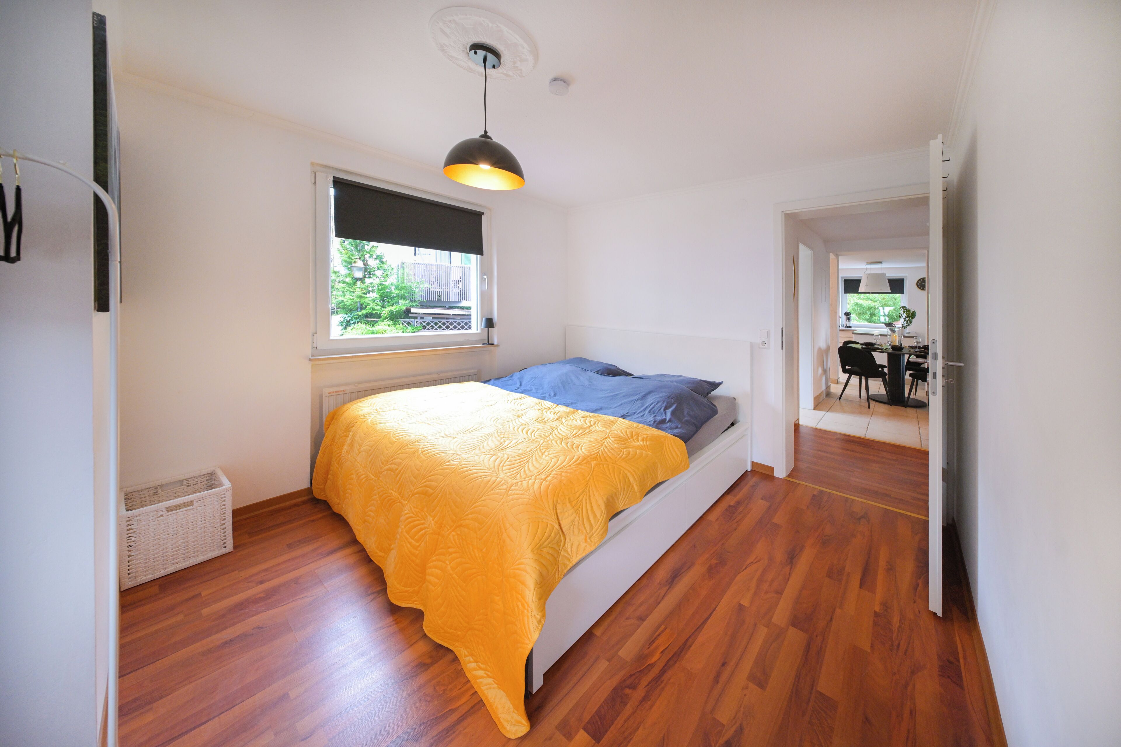 A bedroom with a bed, a window, a hanging light fixture, and a view of the outside.