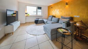 A modern living room with a grey sectional sofa, a flat-screen TV, a round rug, and a small side table with a decorative item.