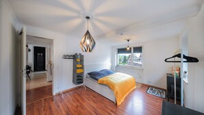 A bedroom with a bed, a hanging light fixture, a window, and a door.