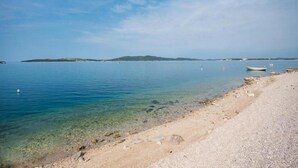 Uma praia com águas cristalinas, areal arenoso e barcos ao longe.