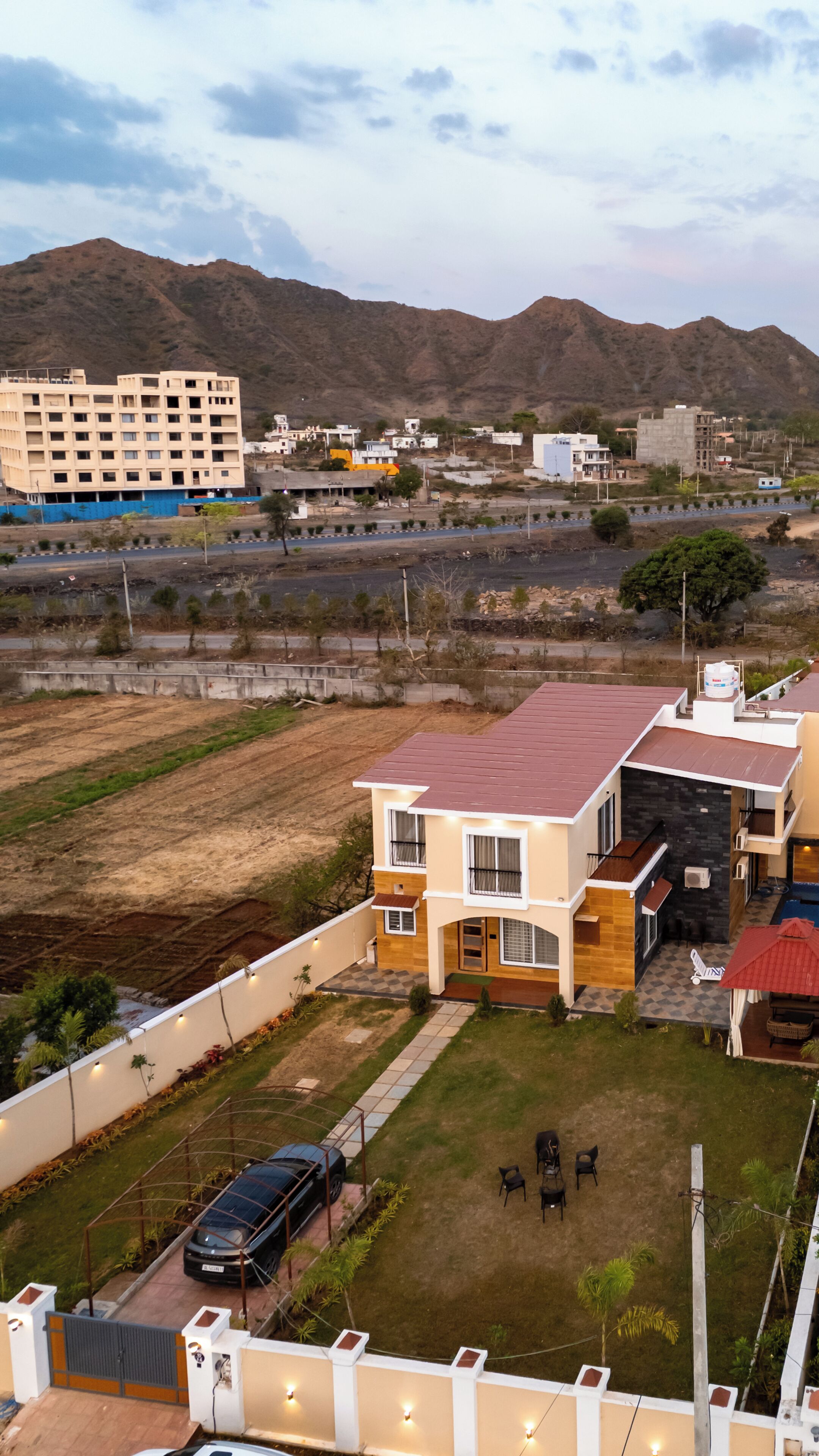 A residential area with a two-story house featuring a red roof, a small front yard, and a parked car.