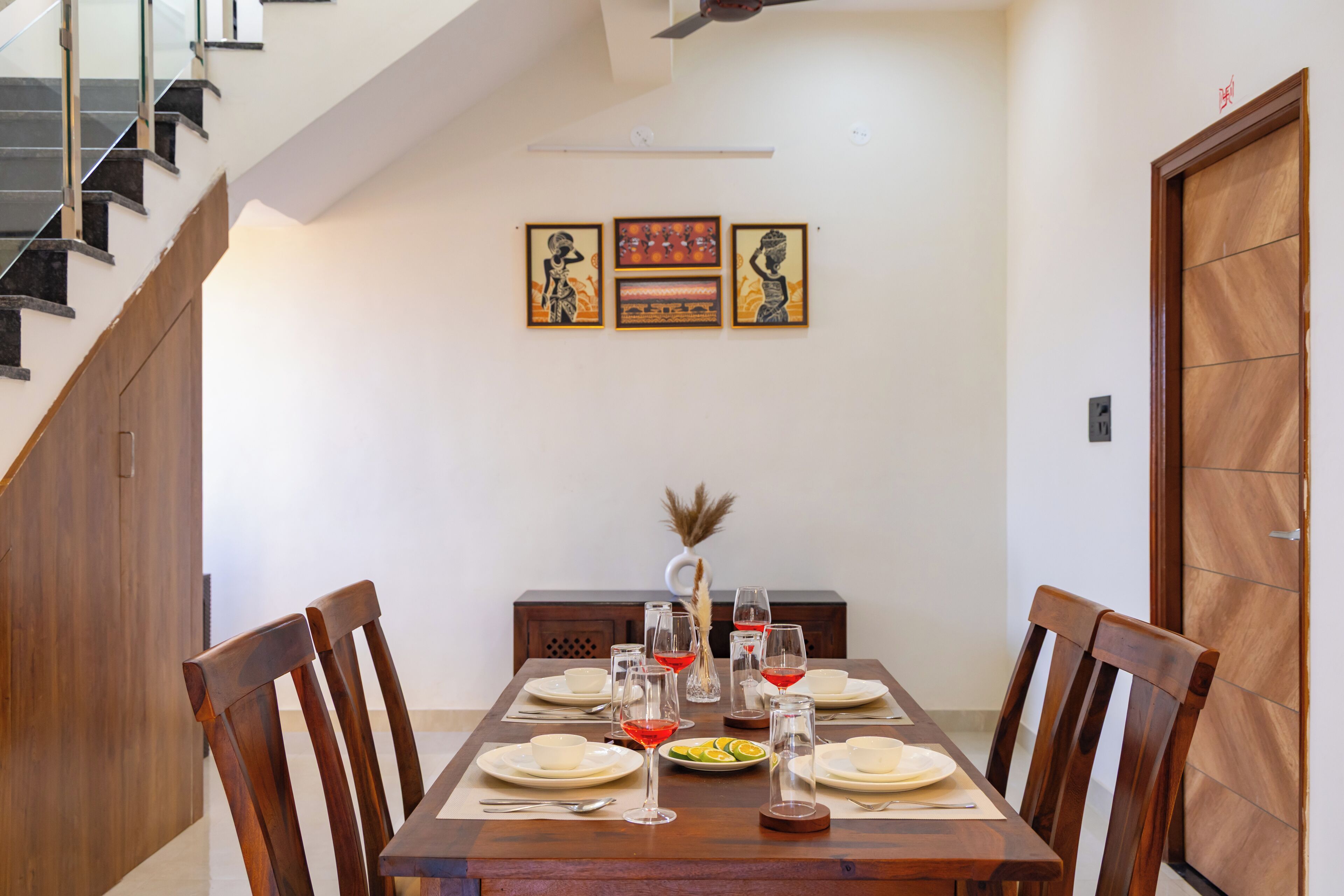Une salle à manger avec une table en bois dressée pour six personnes, des chaises et un escalier sur le côté gauche.