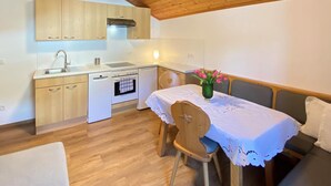 Cocina compacta con armarios de madera, un lavamanos, una estufa y un lavavajillas. Hay una zona de comedor con una mesa cubierta con mantel blanco y un jarrón con flores.