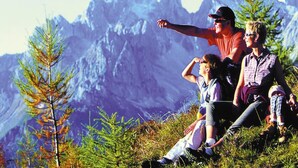 Una familia sentada en una colina cubierta de hierba con montañas al fondo.