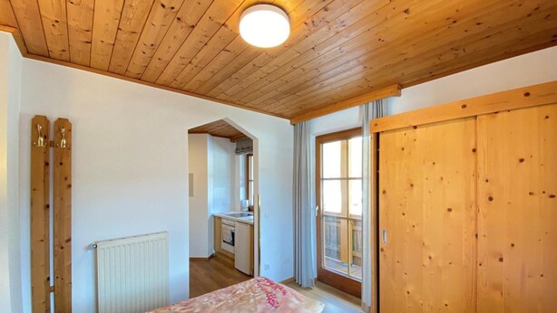 Habitación con techo de madera, cama con ropa de cama floral, armario de madera y vistas a un balcón.
