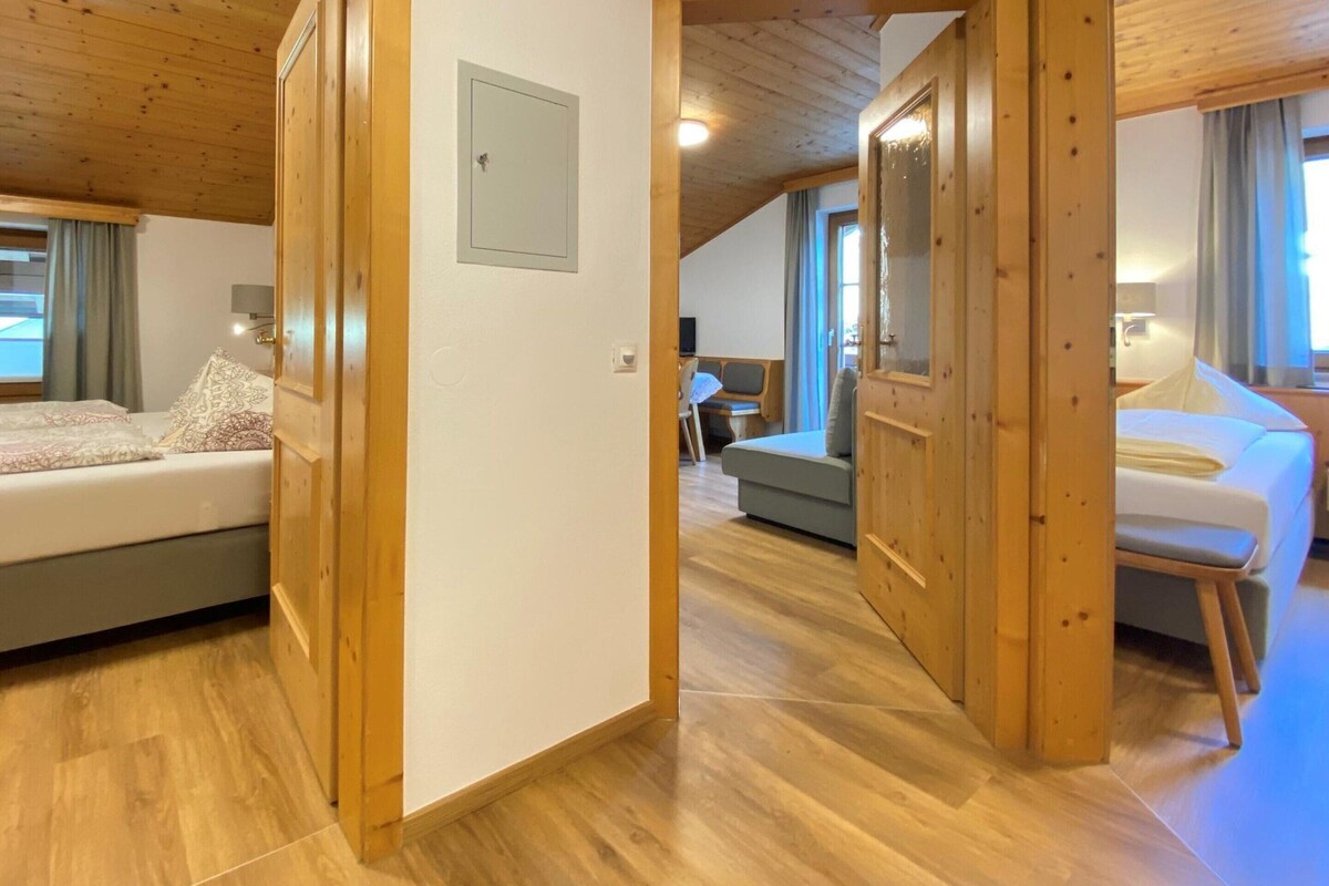 A room with wooden floors, a bed, a sofa, and a dining area with a table and chairs.