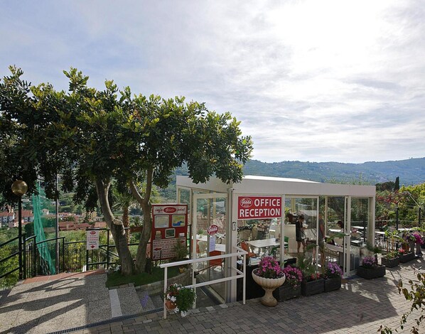 A reception area with a glass enclosure, outdoor seating, and a view of the surrounding landscape. - Ferienwohnung fur 4 Personen in Imperia (Imperia)