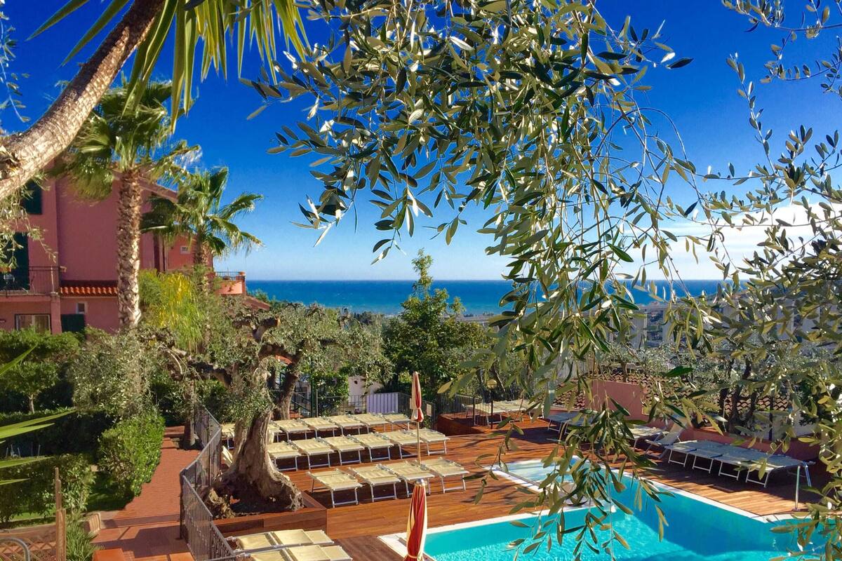 A pool area with lounge chairs and a view of the sea.