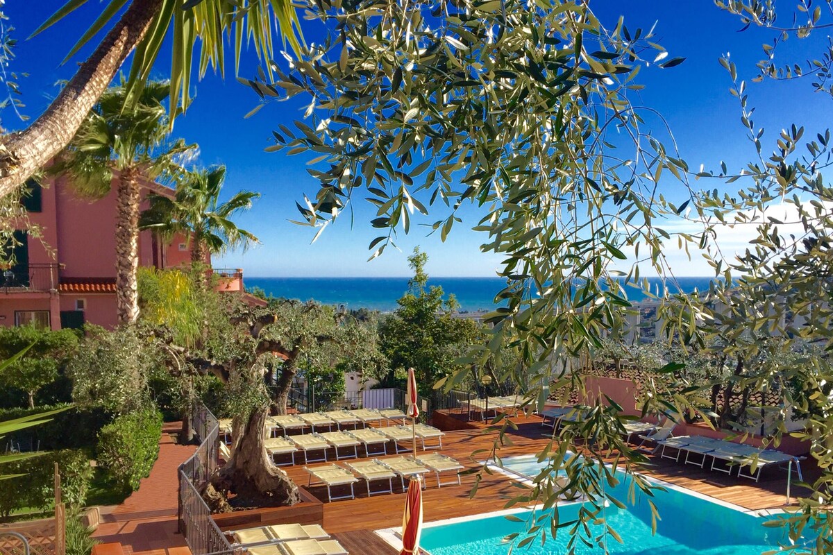 A pool area with lounge chairs and a view of the sea.