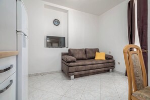 A living room with a sofa, a TV, a clock, and a chair. - Studio in Valbandon Near Brijuni National Park (Fazana)