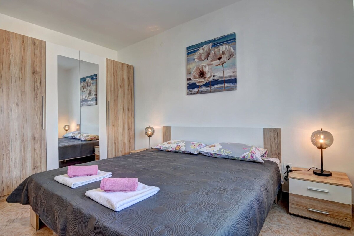 A bedroom with a bed, bedside tables, a mirror, and a painting on the wall.