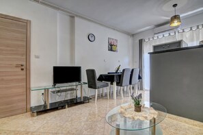 A modern living room with a glass TV stand, dining area with chairs, a clock, and a refrigerator. - Studio in Valbandon Near Brijuni National Park (Fazana)