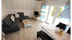 Una sala de estar moderna con un sofá modular, un televisor, una mesa de centro y una zona de comedor con un banco.