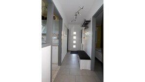 Un pasillo estrecho con un banco, una puerta al final y un candelabro en el techo.