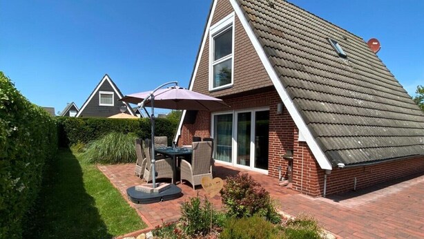 Una casa con fachada de ladrillo, techo de tejas y un patio con mobiliario exterior.