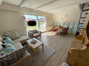 A spacious living room with a sofa, coffee table, and dining area with chairs. - Ferienhaus in Dornumersiel (Dornum)