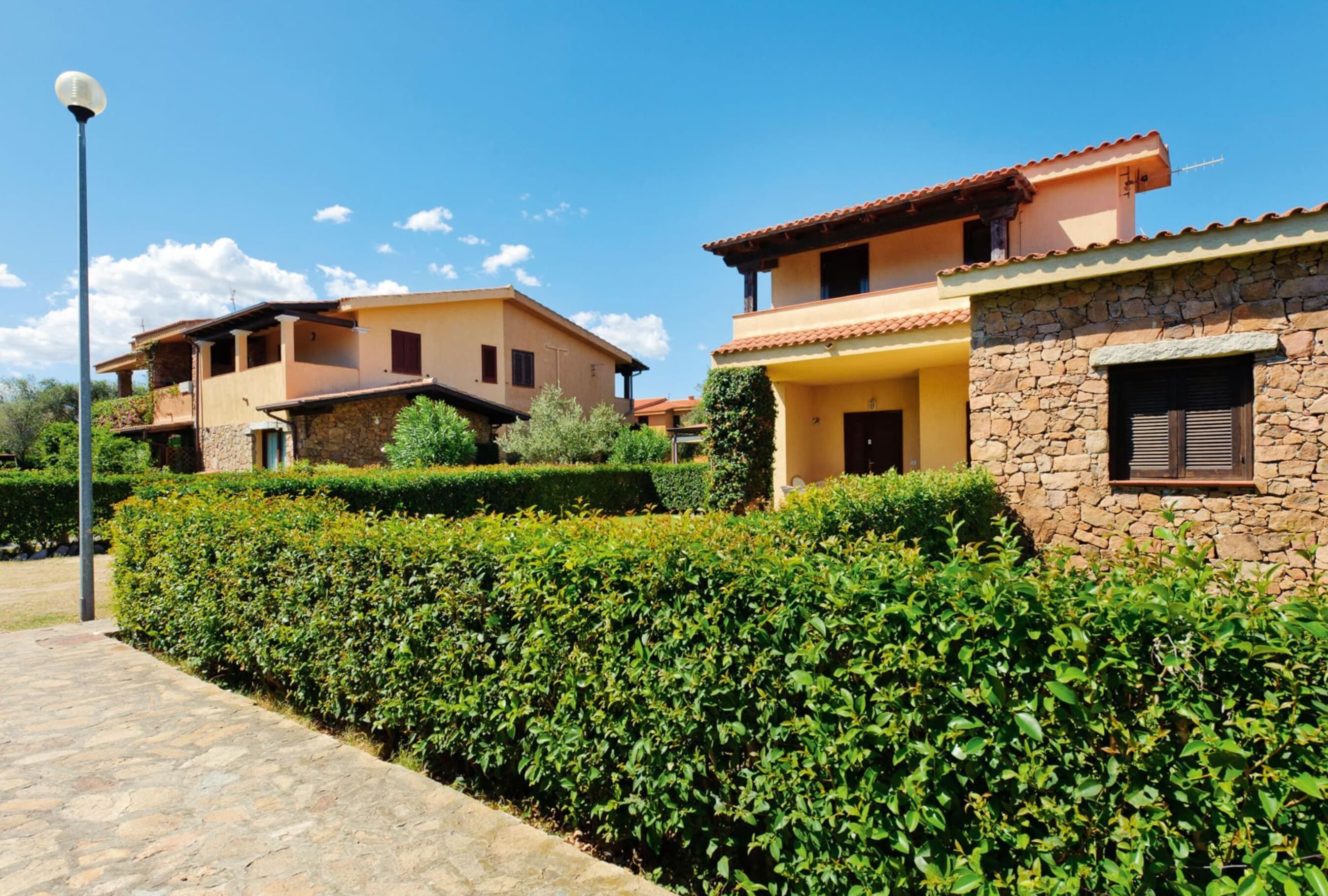 A residential area with stone and stucco buildings, a paved pathway, and well-maintained hedges.
