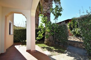 A covered outdoor area with a stone wall, a palm tree, and a pathway leading to a building. - Appartements in San Teodoro Near Centre (San Teodoro)