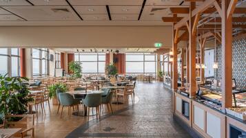 A spacious dining area with multiple tables and chairs, large windows, and a buffet counter.