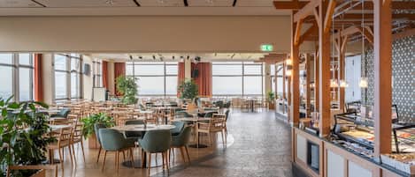 A spacious dining area with multiple tables and chairs, large windows, and a buffet counter.