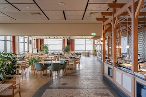A spacious dining area with multiple tables and chairs, large windows, and a buffet counter. - Appartements im Ferienpark in Schoneck (Schoeneck)