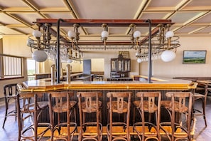 A bar area with wooden chairs, a bar counter, and a chandelier. - Appartements im Ferienpark in Schoneck (Schoeneck)