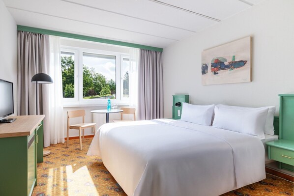 A hotel room with a bed, a desk, a chair, a table, and a window with curtains. - Appartements im Ferienpark in Schoneck (Schoeneck)