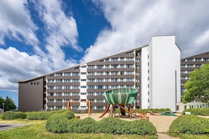 A modern hotel with a multi-story structure, a playground area with a swing set, and a large green chair. - Appartements im Ferienpark in Schoneck (Schoeneck)