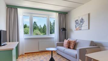 A room with a sofa, a small table, a TV on a stand, and a window with curtains.