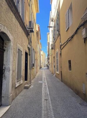 Eine enge Kopfsteinpflasterstraße, gesäumt von Gebäuden mit Rundbögen und Fensterläden.
