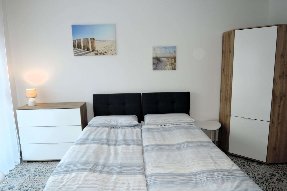 Een slaapkamer met een bed, een nachtkastje met een lamp, een kledingkast en twee aan de muur hangende foto's.