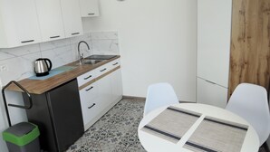 Una cucina compatta con mobili bianchi, un lavello e una sveglia al muro.