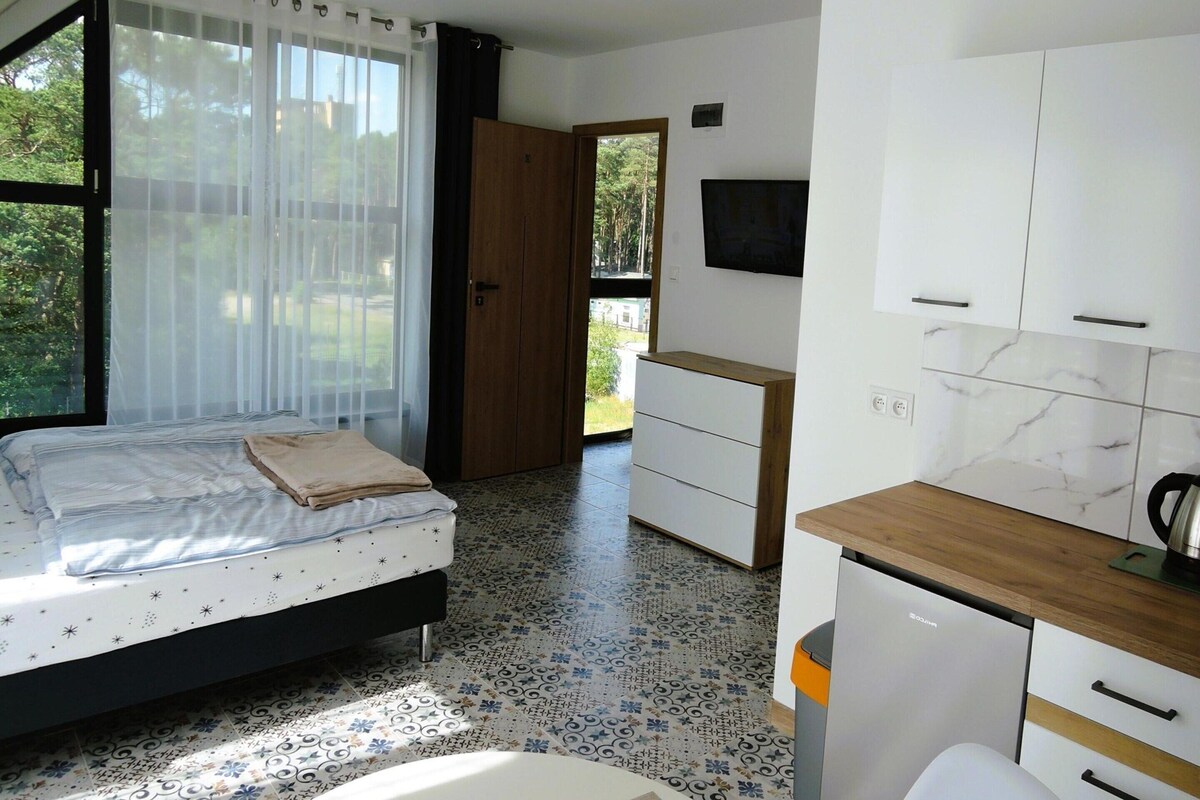Een slaapkamer met een bed, een houten deur, een badkamer met een wastafel en toilet, en een keuken met kastjes en een aanrecht.