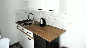 Una cucina compatta con mobili bianchi, un piano di lavoro in legno, un lavello e un bollitore.
