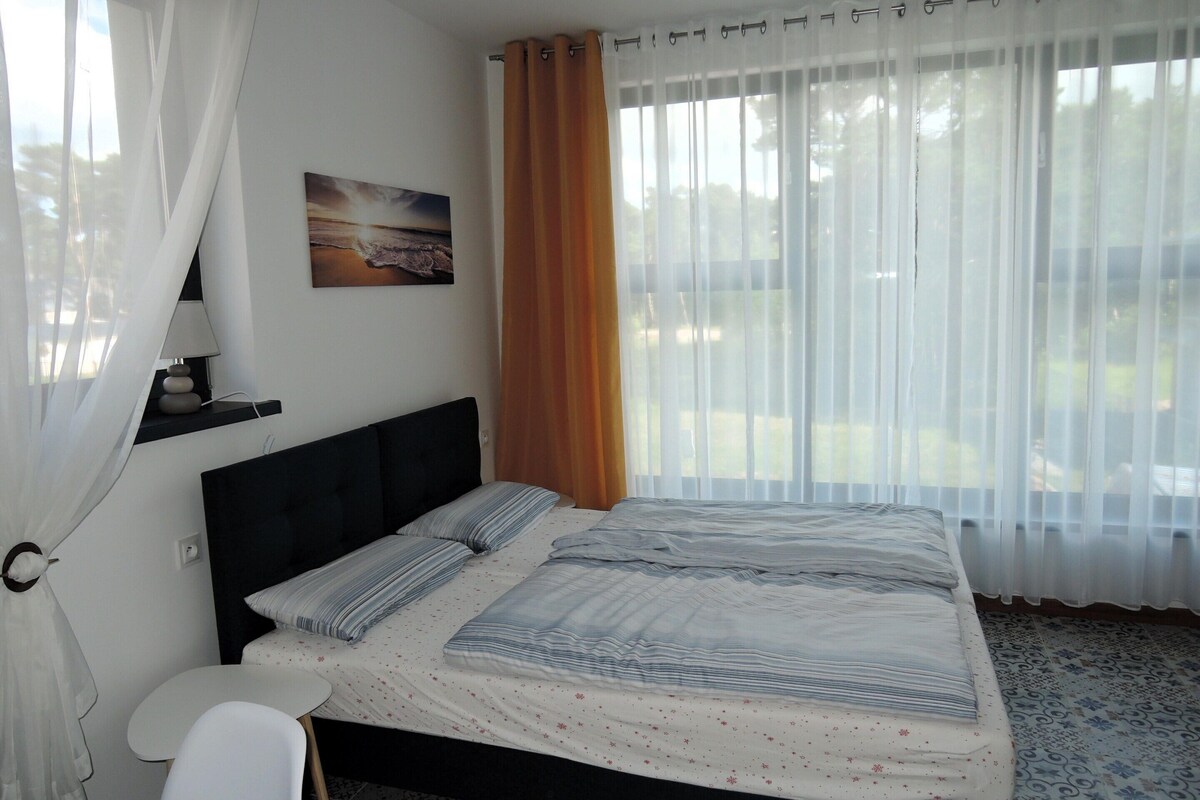 Een net opgemaakt bed met gestreepte lakens, een nachtkastje en een wandlamp.