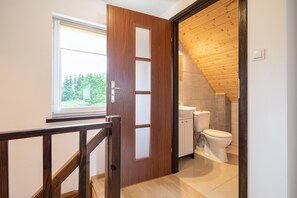 A wooden door leading to a bathroom with a toilet and sink, a window, and a wooden ceiling. - Brick Cottage Near Baltic Sea and Windmill (gmina Karnice)