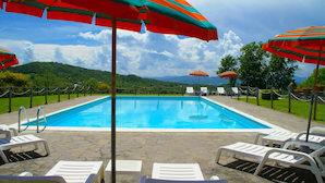 A swimming pool with lounge chairs and striped umbrellas, surrounded by a stone deck and a view of green hills. - Holiday Home in Citta di Castello With Pool (Città di Castello)