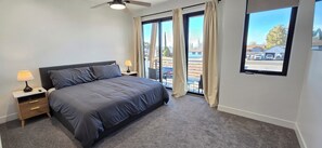 Une chambre à coucher comprenant un lit, des tables de chevet, un ventilateur de plafond et de grandes fenêtres avec des rideaux.