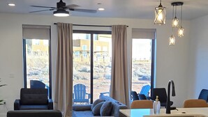 A modern living room with a sofa, chairs, a dining area with a kitchen island, and large windows with curtains. - Antelope Canyon Comfy Townhouse - Sleeps 11 (Page)