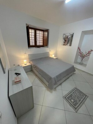 Une chambre à coucher avec un lit, des tables de chevet, une fenêtre, un tableau et une plante décorative.