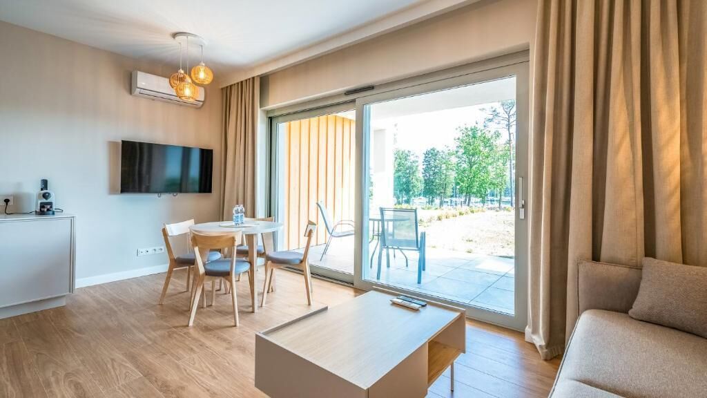 A modern living room with a sofa, a coffee table, a TV, and a dining area with chairs.