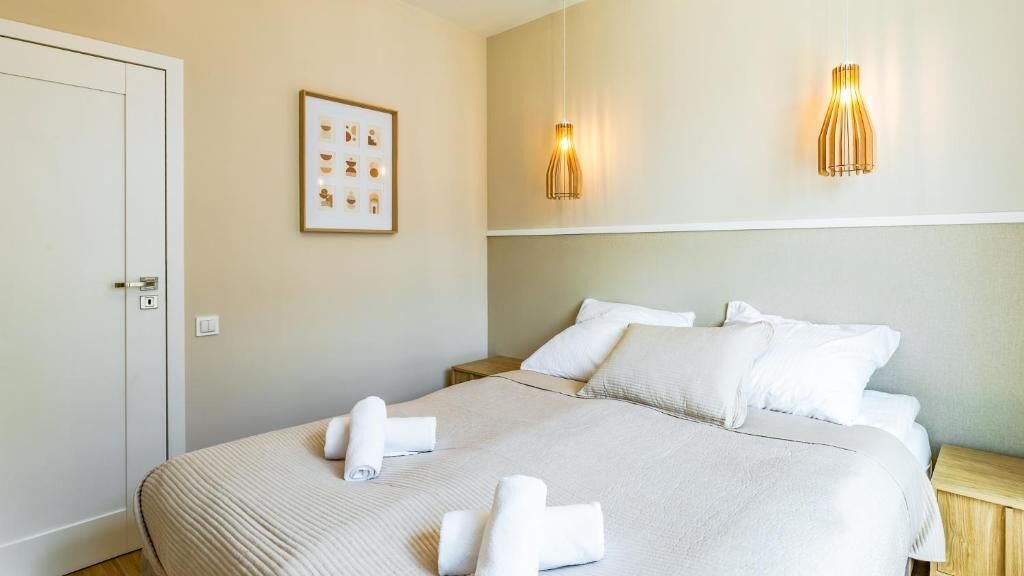 A neatly made bed with white linens and towels, a framed picture on the wall, and two wall-mounted lamps.