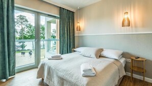 A hotel room with a bed, a small table, a lamp, and a view of the outdoors. - Stranda Residence Apartments Giżycko (Giżycko)