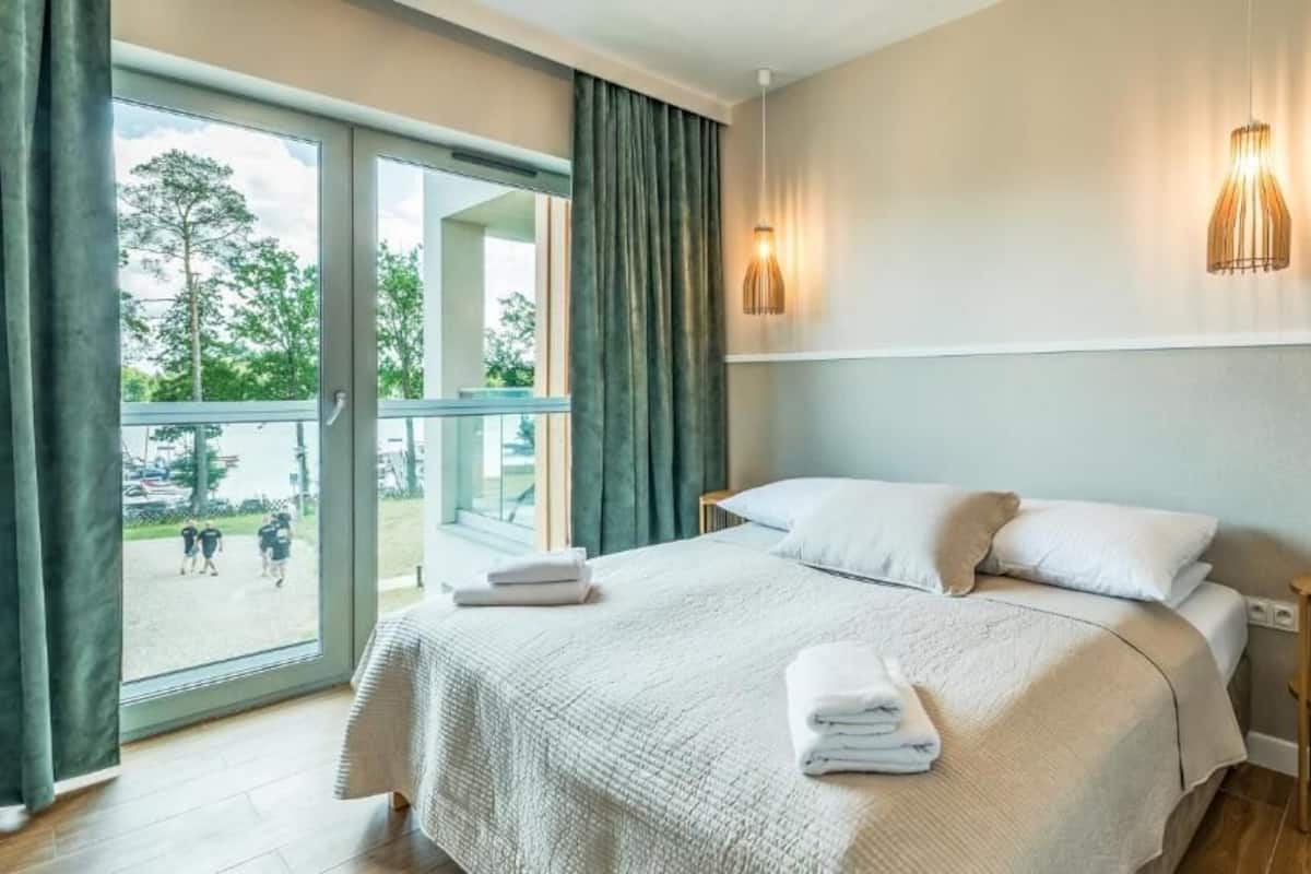 Ein Hotelzimmer mit Bett, kleinem Tisch, Lampe und Blick ins Freie.